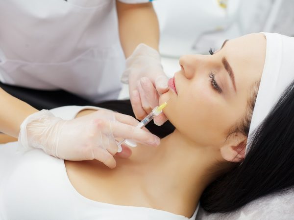 Woman receiving a botox injection in the lips zone lying in bathrobe on the medical couch